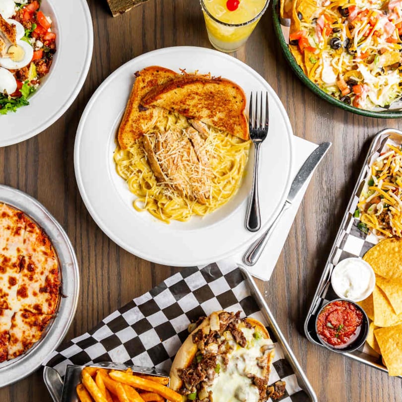 Overhead view of various sports bar dishes, including pasta, nachos, pizza, and a cheesesteak.
